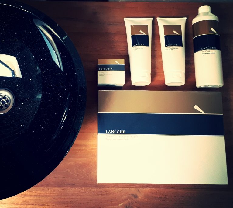 Lan&eacute;che verzorgingsproducten op een houten blad naast de zwarte waskom in Salon Romy